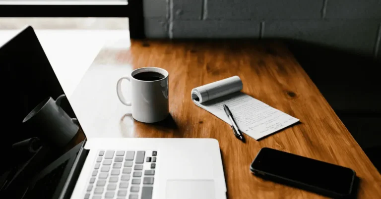 Banking for Gen Z. A modern workspace featuring a laptop, coffee mug, notepad, and smartphone, representing the digital solutions for banking catered to Gen Z, as discussed on PoppaSaid.com.