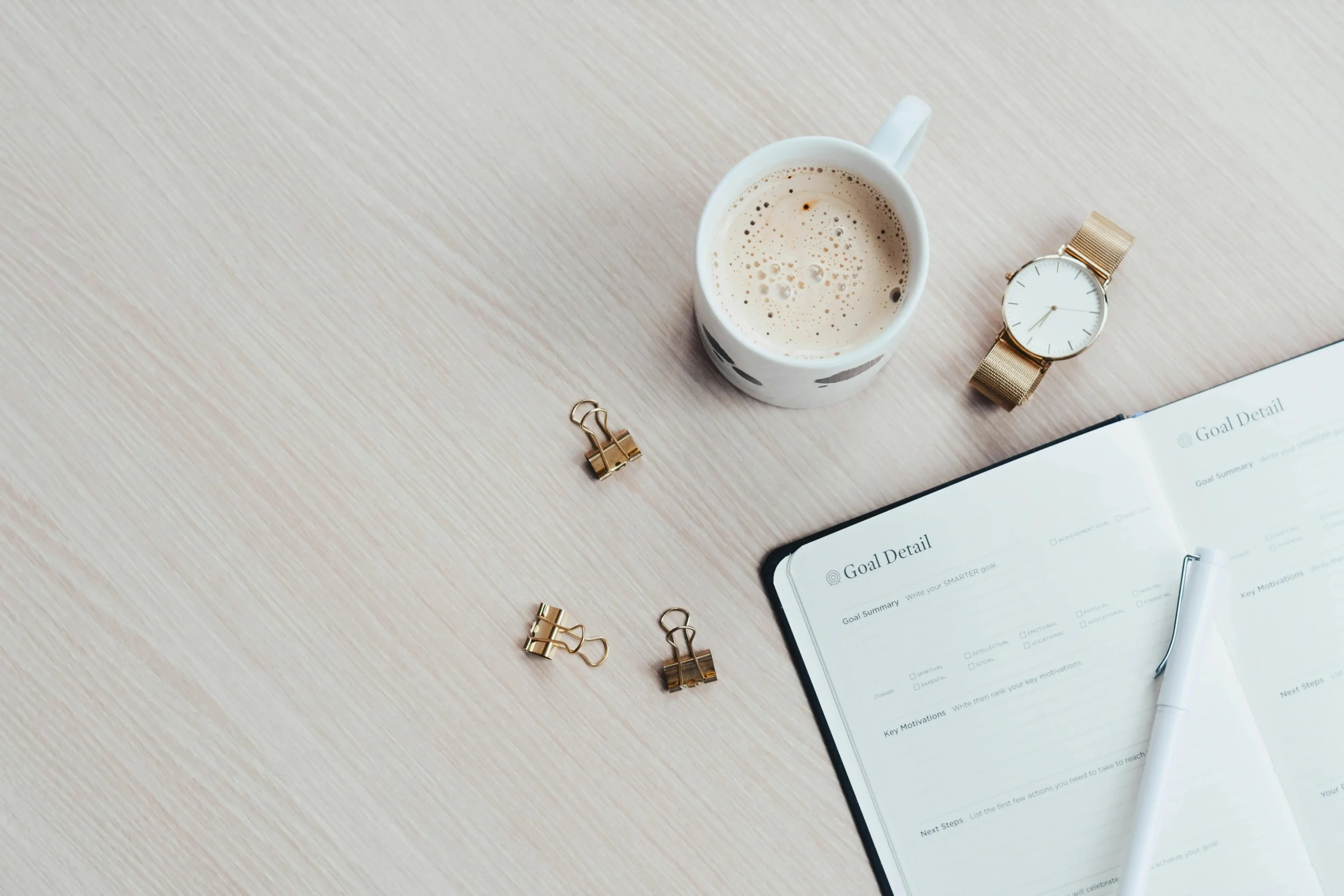 Top-down shot of a cup of coffee, watch, binder clips, and planner with a pen, symbolizing time management tips.