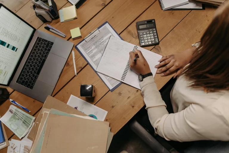 Overhead shot of someone using a laptop and reviewing paperwork, representing budgeting tools for 2024.
