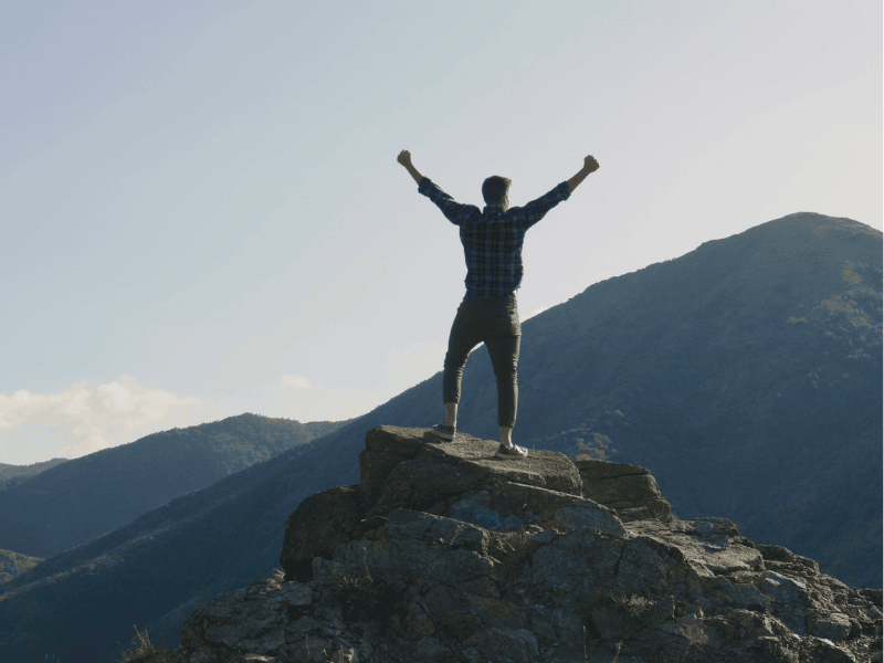 Man on mountaintop raising arms – emotional clarity and financial empowerment